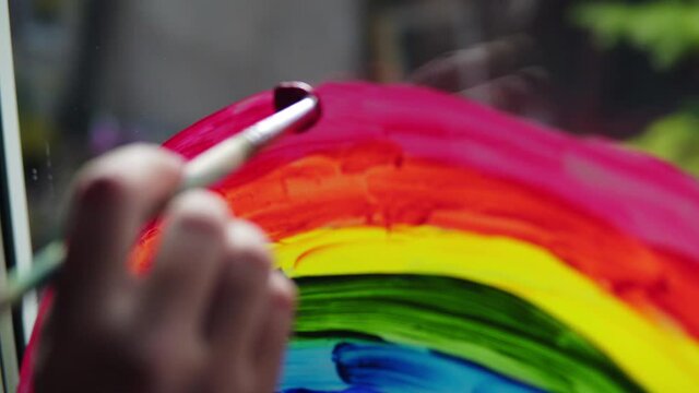 Painting a rainbow with paints on a window close-up