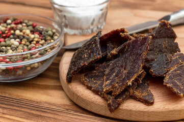Beef jerky with salt and pepper on cutting board. Dried meat with spices.