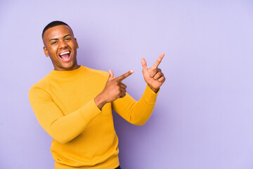 Young latin man isolated on purple background pointing with forefingers to a copy space, expressing excitement and desire.