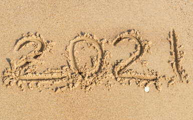 Year 2021 written on sand of sea beach.