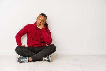 Young latin man sitting on the floor isolated who feels sad and pensive, looking at copy space.