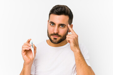 Young caucasian man holding a thermometer isolated Young caucasian man holding  a pointing his temple with finger, thinking, focused on a task.