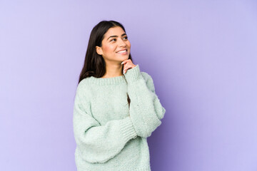 Young indian woman isolated on purple background relaxed thinking about something looking at a copy space.