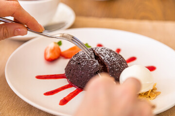 The girl cuts the chocolate fondant with a knife. Chocolate dessert, plate decorated with jam and strawberry wedge.