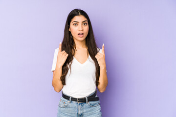 Young indian woman isolated on purple background pointing upside with opened mouth.