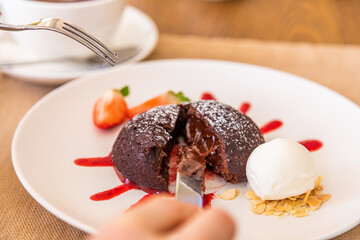 The girl cuts the chocolate fondant with a knife. Chocolate dessert, plate decorated with jam and strawberry wedge.