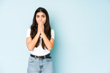 Young indian woman on blue background shocked, covering mouth with hands, anxious to discover something new.