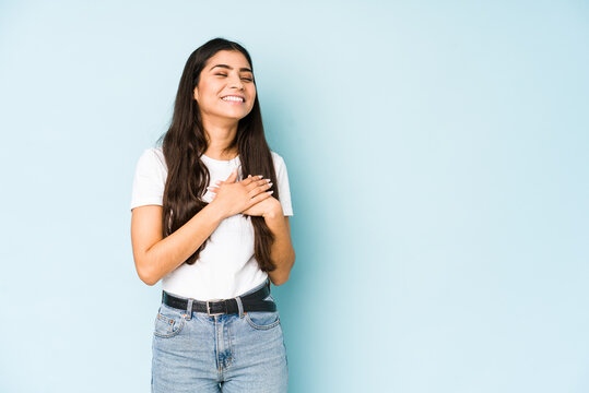 Young indian woman on blue background laughing keeping hands on heart, concept of happiness.