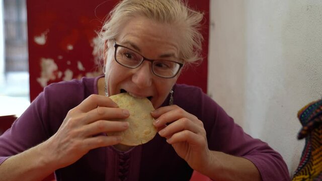 Pretty tourist woman picks up a gorditas and takes a bite in a small Mexican restaurant.