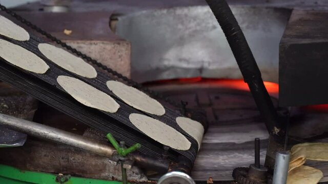 Tortillas stamped out into perfect circles move down a conveyor belt towards the oven where they are cooked.
