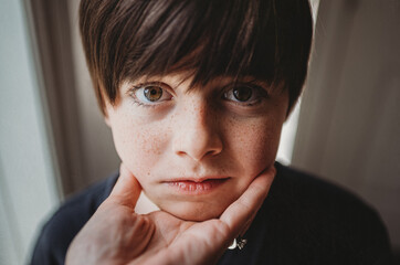 Close up of young boy's face being held under his chin by a hand.