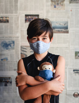 Portrait of boy wearing face mask holding toy monkey against newspaper clippings