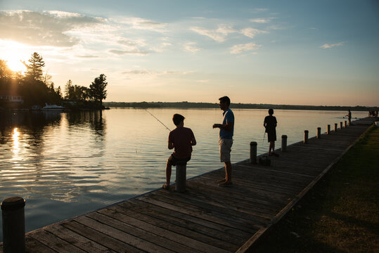 Father and sons fishing on dock of lake at sunset in Ontario, Canada.