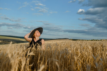 Woman in black dress and hat is lying on the wheat in the wheat field.