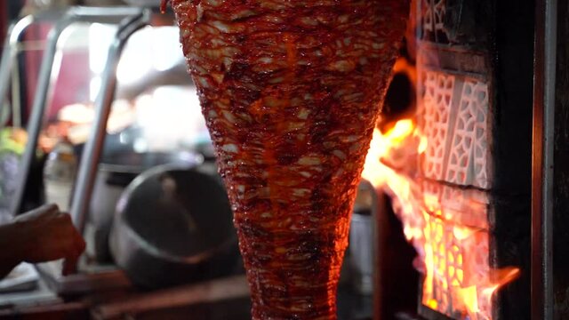 Slow motion of fire cooking al Pastor and a hand turning the Mexican specialty pork dish which is fast food street food.