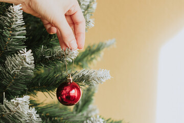 Anonymous person hanging red bauble on branch of Christmas tree home