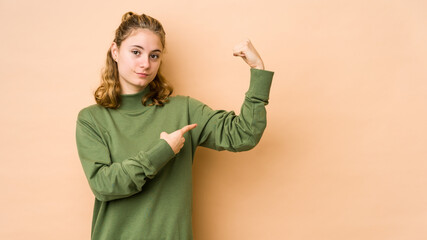 Young caucasian woman isolated on beige background showing strength gesture with arms, symbol of feminine power