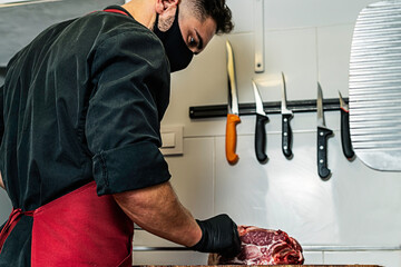 Butcher with mask cutting raw meat in the wood