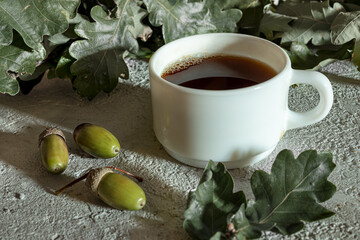 Cup of acorn coffee, acorns and green oak leaves on a gray background. An alternative to traditional coffee, a healthy homemade eco-friendly hot drink with a coffee flavor and without caffeine. © t.sableaux