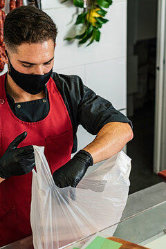 Professional Butcher with mask putting goods into a plastic bag