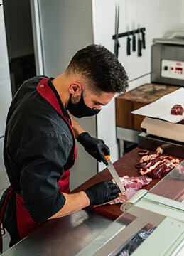 Professional butcher with mask cutting raw meat