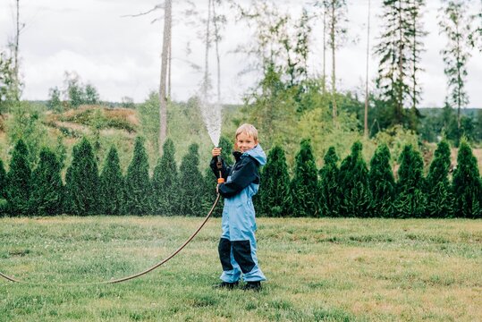 boy standing with a hose spraying water at home in the yard