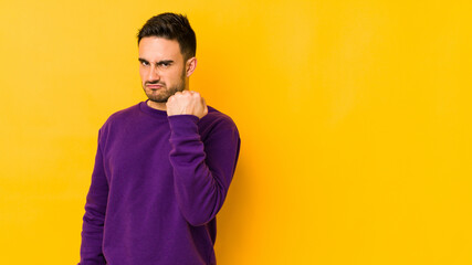 Young caucasian man isolated on yellow bakground showing fist to camera, aggressive facial expression.