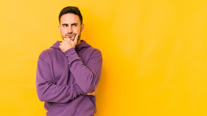 Young caucasian man isolated on yellow bakground looking sideways with doubtful and skeptical expression.