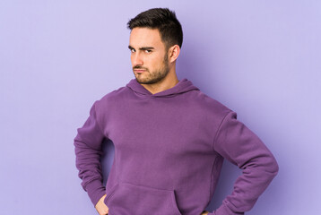 Young caucasian man isolated on purple background frowning face in displeasure, keeps arms folded.