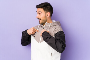 Young caucasian man isolated on purple background surprised pointing with finger, smiling broadly.
