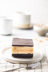 Piece of cake with souffle Birds milk, biscuit, mousse and dark chocolate on a white plate, light background