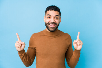 Young latin man against a blue  background isolated indicates with both fore fingers up showing a...