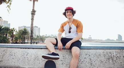 Portrait of funny male teenager dressed in youthful clothing smiling at camera during leisure resting, handsome Caucasian hipster guy in trendy apparel posing during good day for recreation