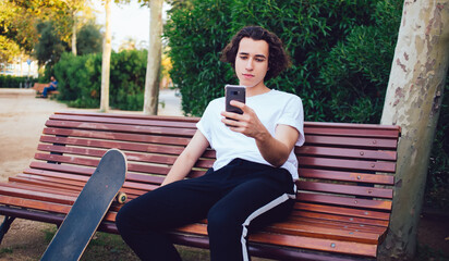 Guy with skateboard browsing smartphone in park