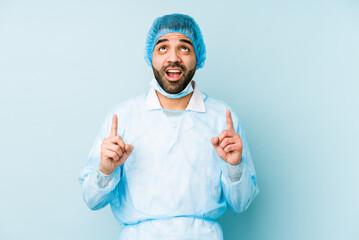 Young surgeon latin man isolated Young dpointing upside with opened mouth.