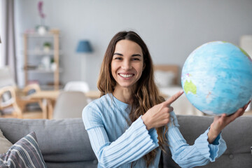 Woman dreaming about travel, pointing with index finger at globe. Planning vacation.