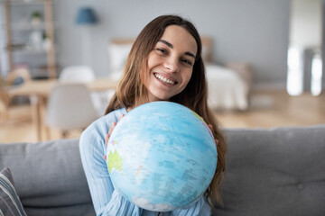 Smiling woman holding a globe in her hands sitting on the couch.