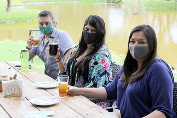 group of latin friends with protection mask eating and drinking in outdoor restaurant, new normal