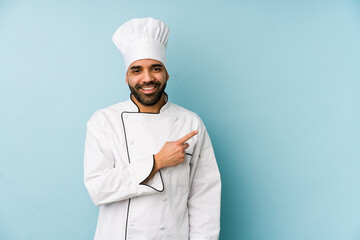 Young latin chef man isolated smiling and pointing aside, showing something at blank space.