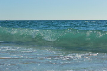 Transparent blue sea wave running to the shore with a crest