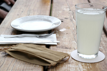 
New normal in restaurants, view rustic wooden table with plate and cutlery accompanied protection mask and antibacterial gel