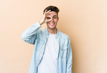 Young caucasian man isolated on beige background excited keeping ok gesture on eye.