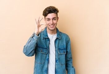 Young caucasian man isolated on beige background cheerful and confident showing ok gesture.