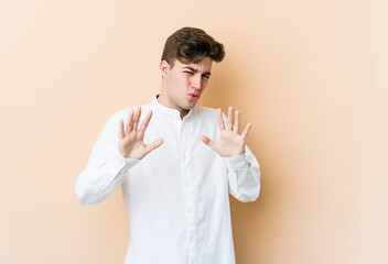 Young caucasian man isolated on beige background rejecting someone showing a gesture of disgust.