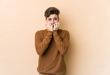 Young caucasian man isolated on beige background biting fingernails, nervous and very anxious.