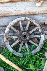The wheel of an old cart against the background of a log wall of an old house.