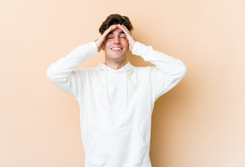 Young caucasian man isolated on beige background laughs joyfully keeping hands on head. Happiness concept.