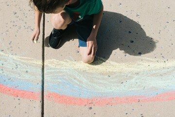 Young boy drawing sidewalk chalk rainbows