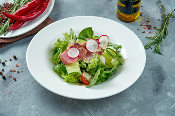 Appetizing nicoise salad with fresh tuna, radish, cucumber in a white plate on a gray background