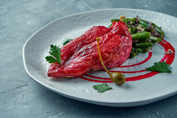 Baked chicken fillet in berry sauce with asparagus garnish with peanuts in a white plate on a gray background